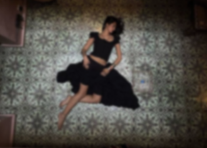 Person in a black dress lying on a patterned rug with a decorative metal gate above.